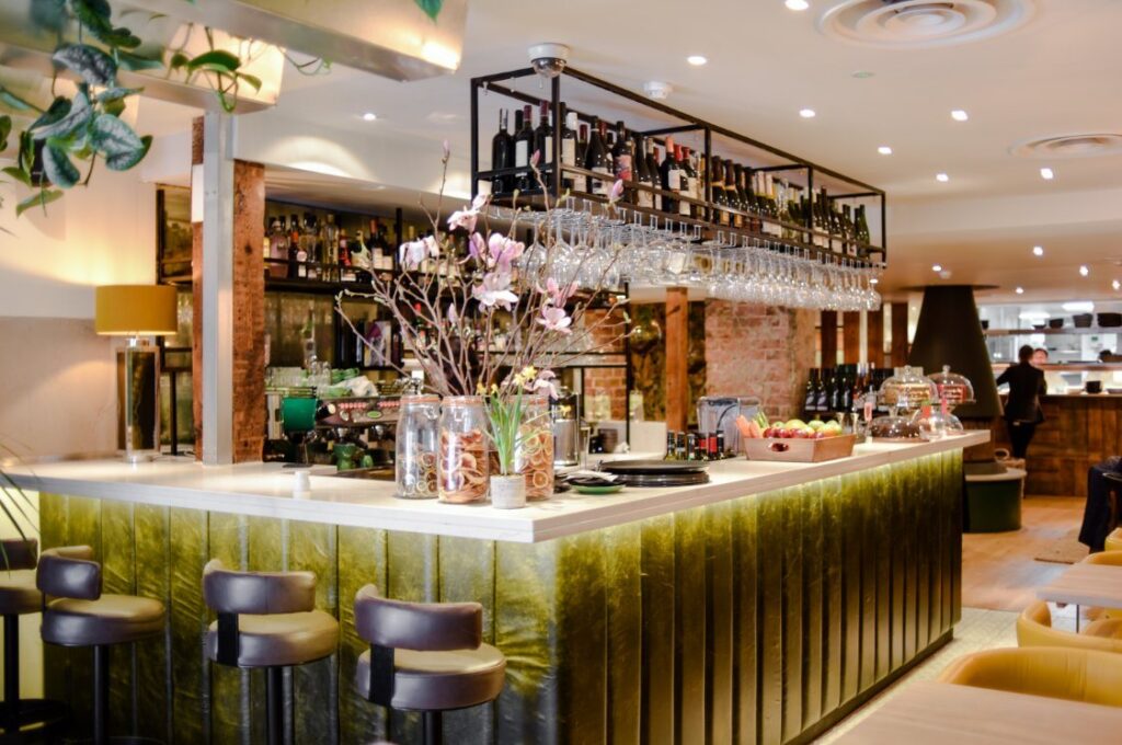 The central bar at Antipodea Richmond, with a green tiled front, leather stools and a back bar of wine