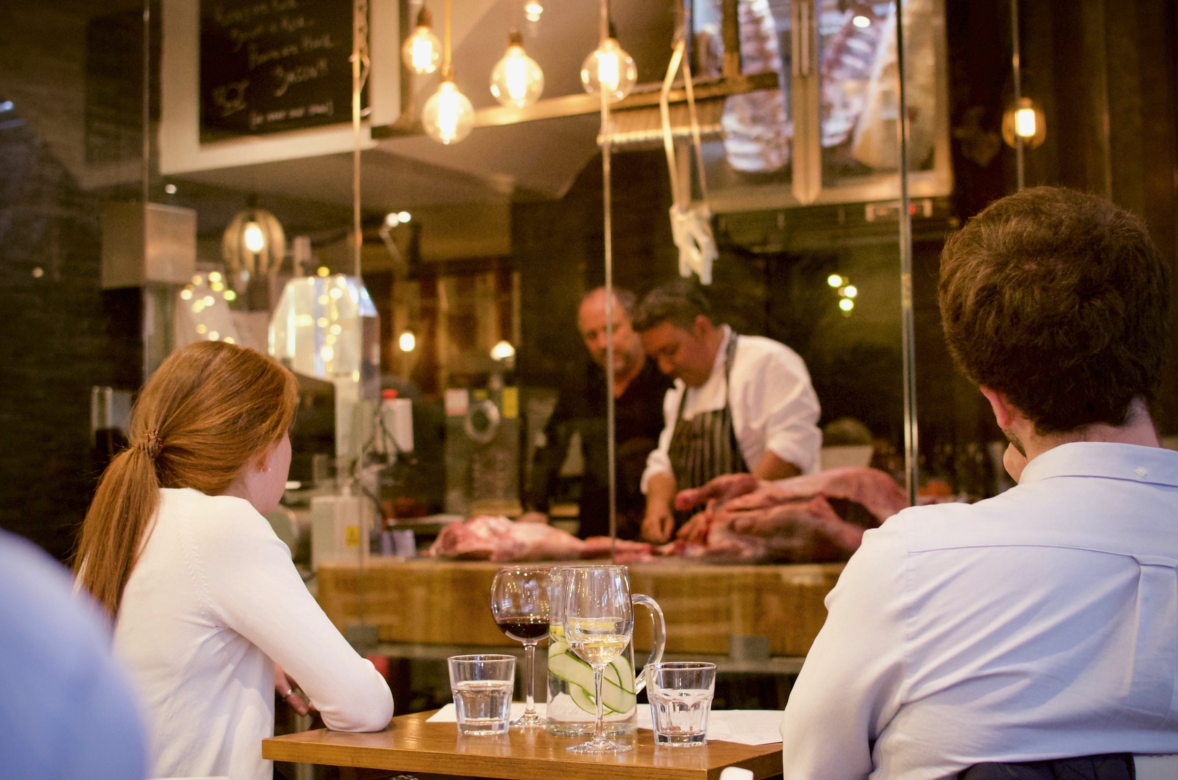 Guests at the counter of Antipodea Richmond watching chefs prepare meat in the open kitchen
