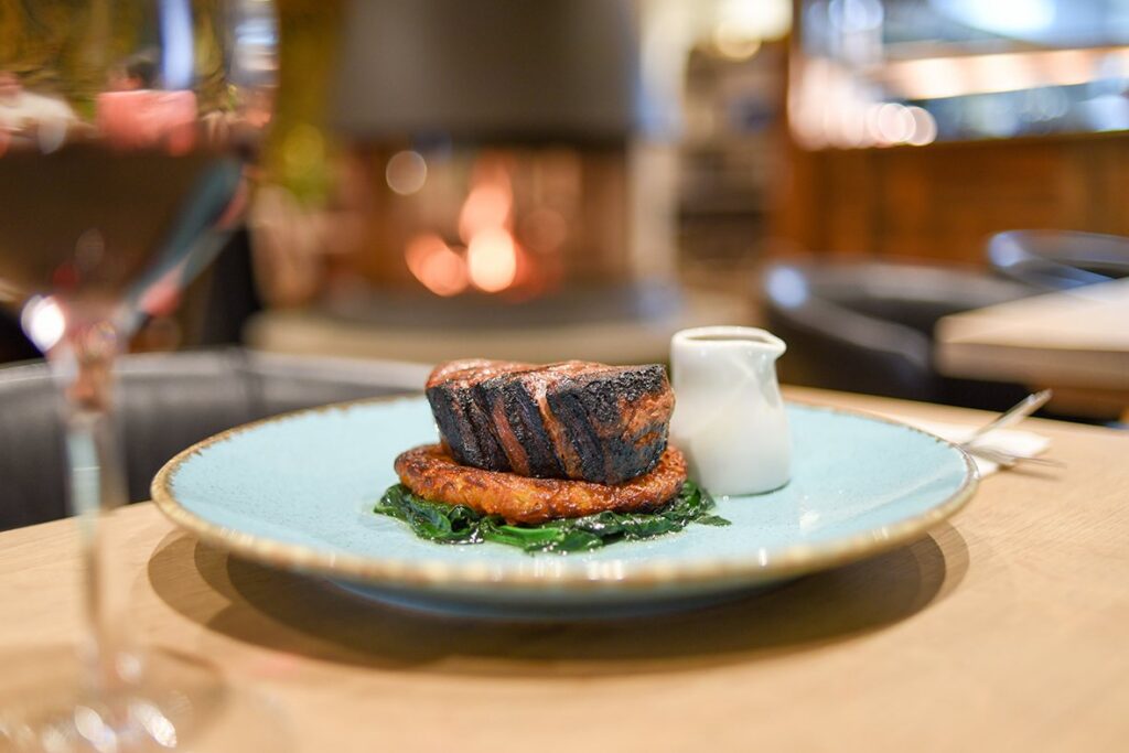 A steak on a pale blue plate, served with greens