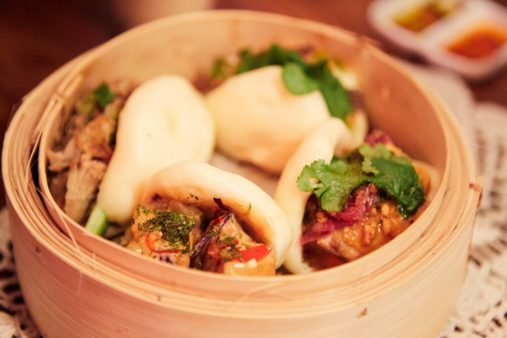 Bao buns filled with braised pork and herbs in a bamboo steamer