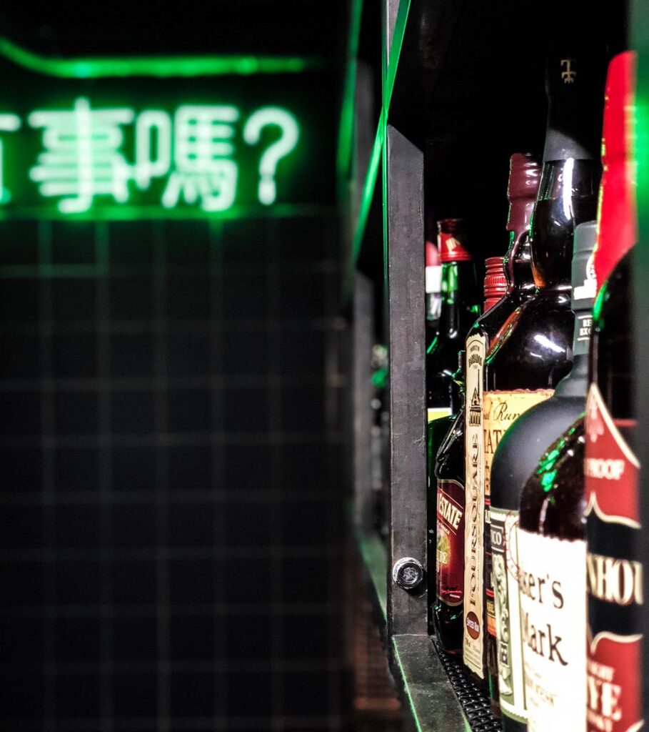 Green neon Taiwanese characters above the bottles in the basement bar