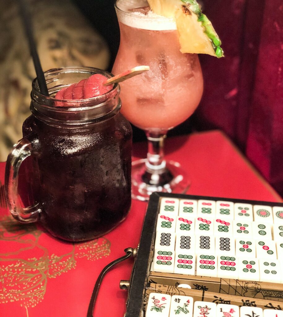 Two cocktails beside an open case of mahjong tiles