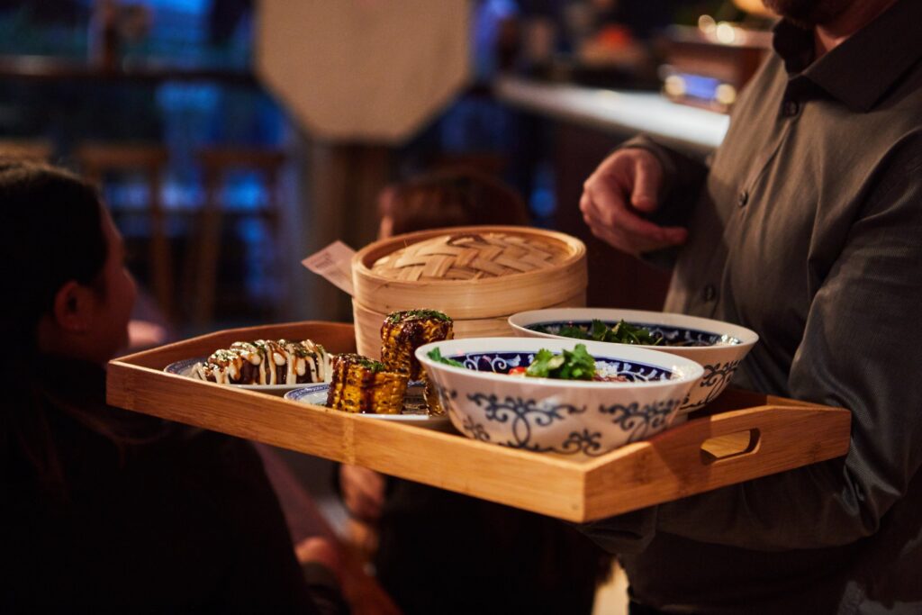 A server carrying a tray of bao and bowls to the table