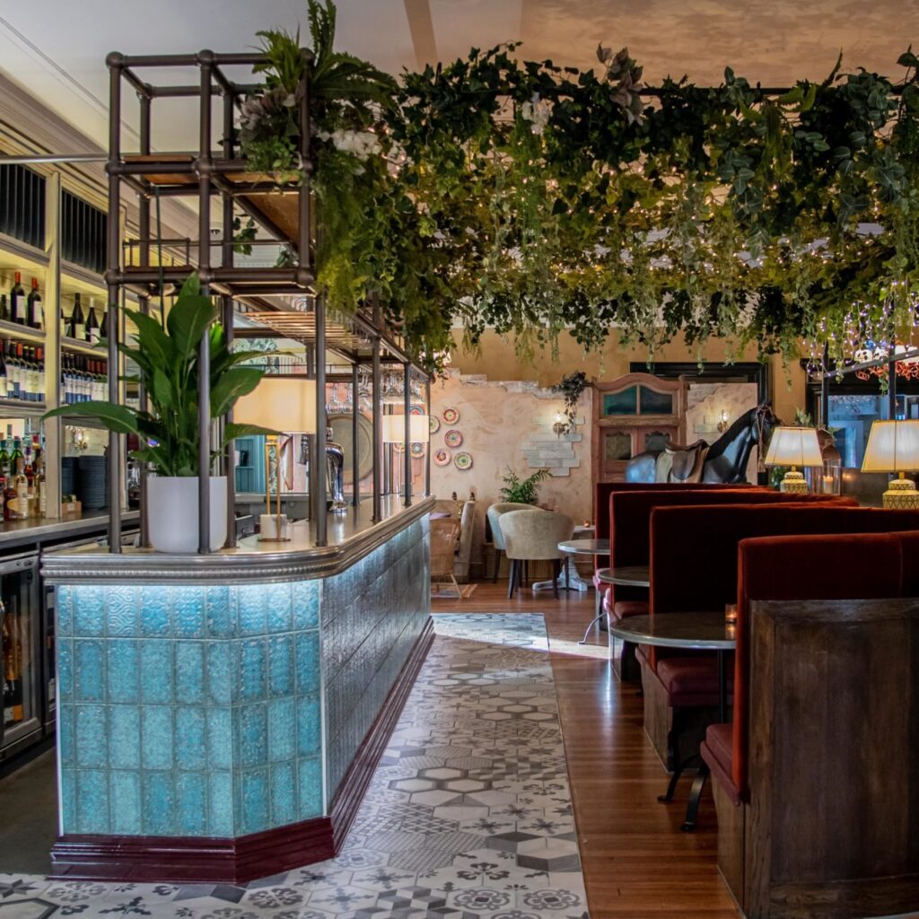 The turquoise tiled bar and booth seating under hanging greenery at Boho Marché
