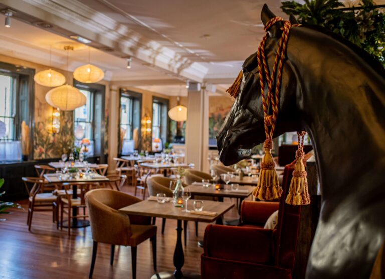 The Boho Marché dining room in Bath, with a life-size horse sculpture, rattan lights and tall Georgian windows