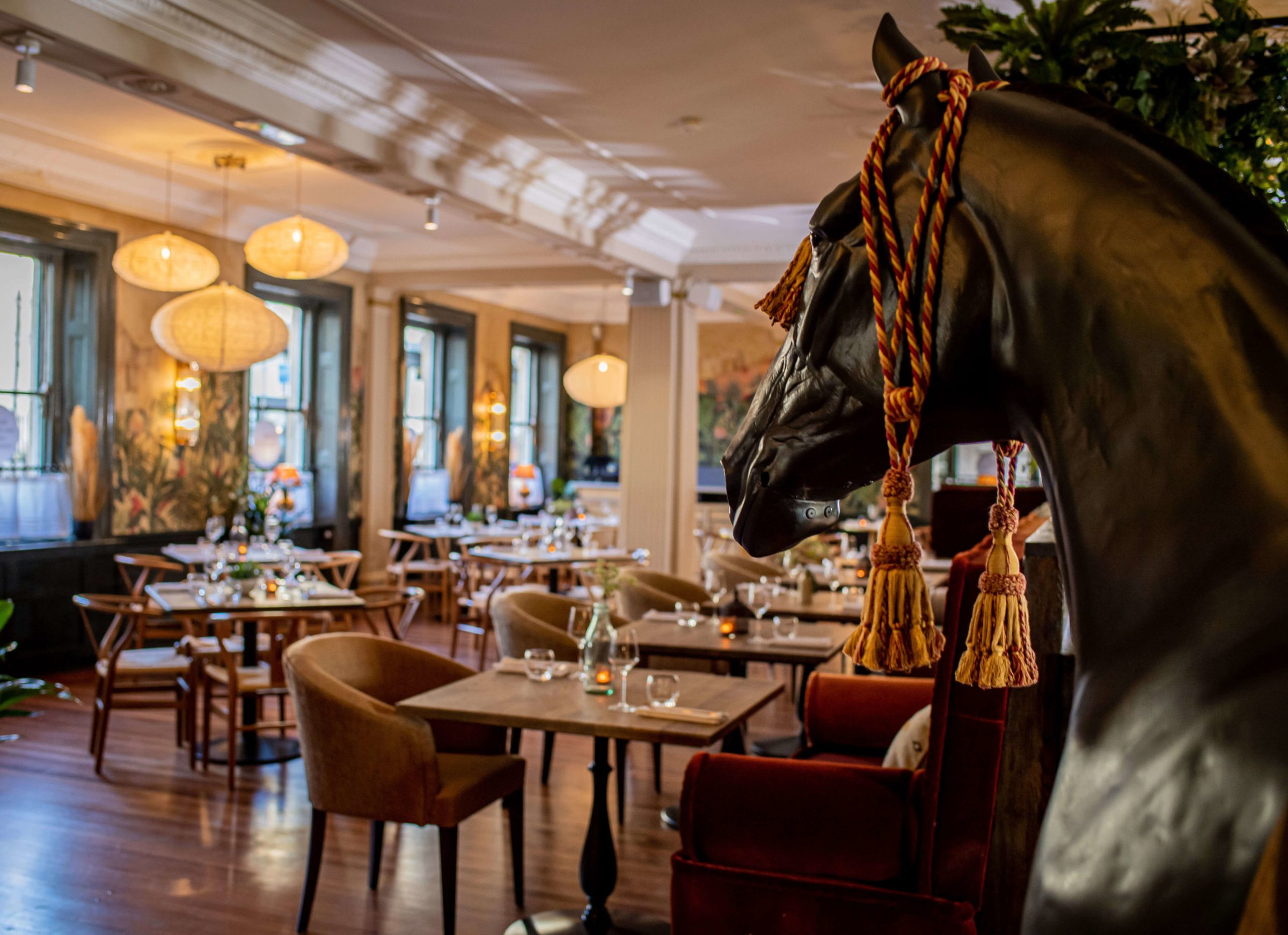 The Boho Marché dining room in Bath, with a life-size horse sculpture, rattan lights and tall Georgian windows