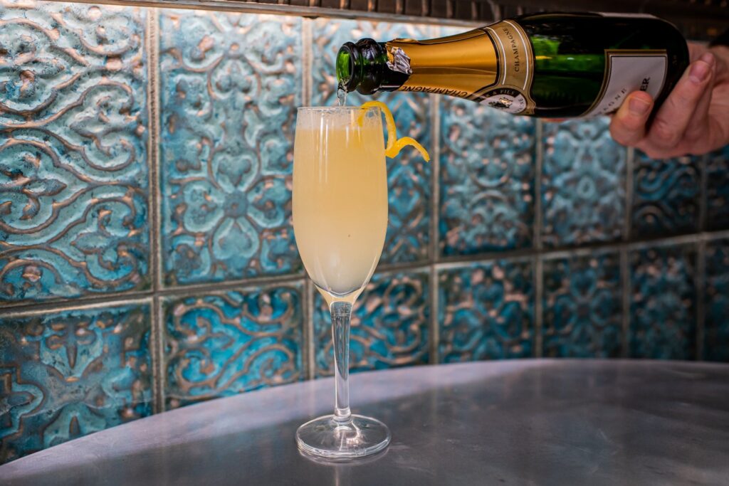 Champagne poured into a cocktail against embossed teal tiles