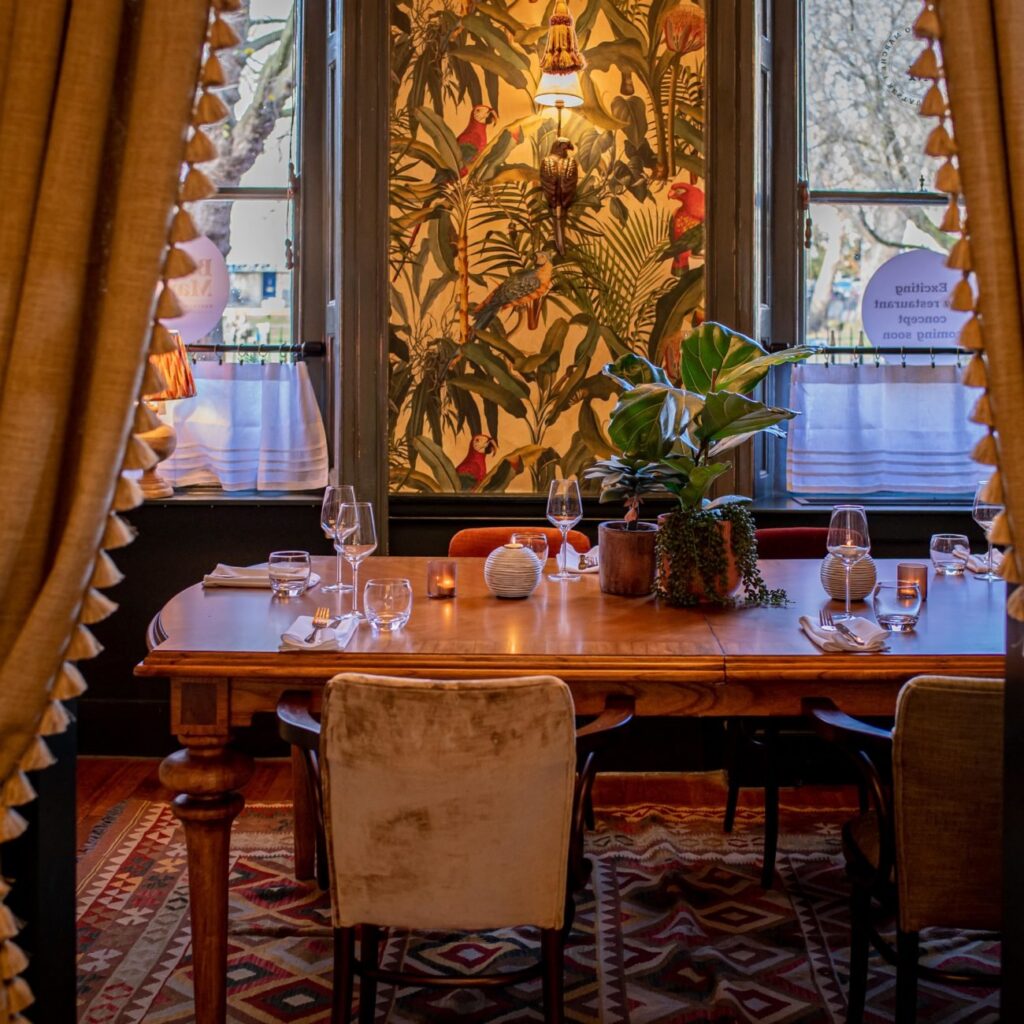 La Mesa, the private dining room at Boho Marché, framed by gold curtains and botanical wallpaper