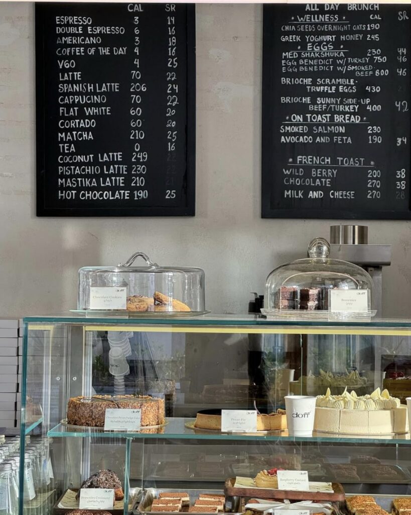Cakes and pastries in the Doff Coffee display counter beneath chalkboard menus