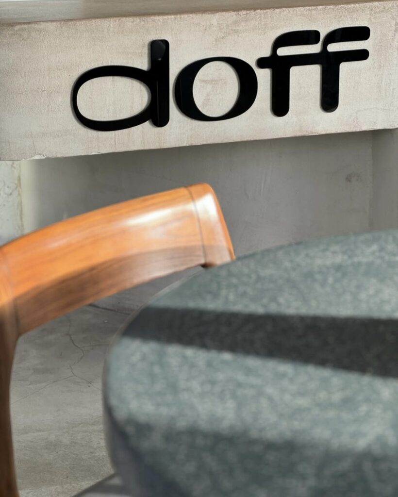 The Doff logo on a concrete wall above a timber chair
