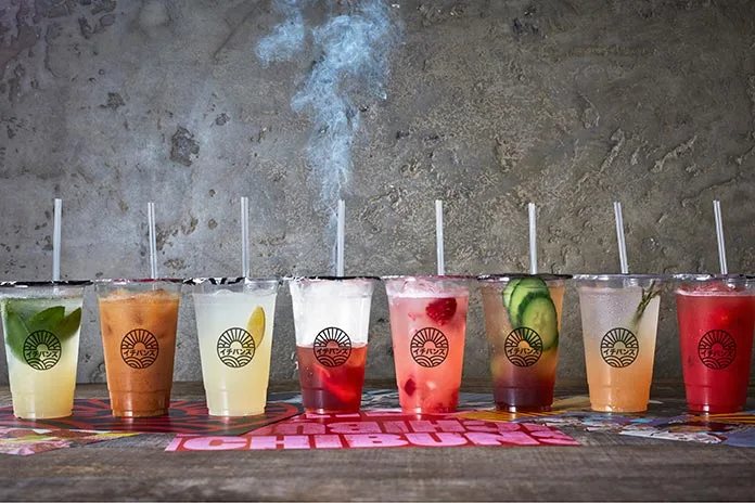 A row of colourful house drinks in branded cups