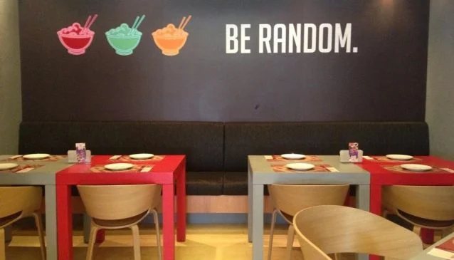 Red and timber tables beneath the Be Random wall graphic at Pan Jan