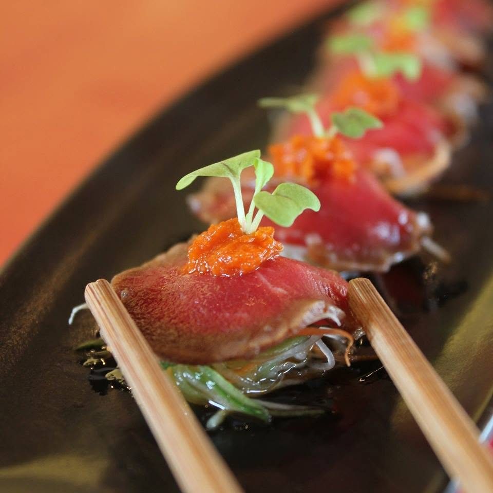 Seared beef nigiri topped with roe and microgreens, held with chopsticks