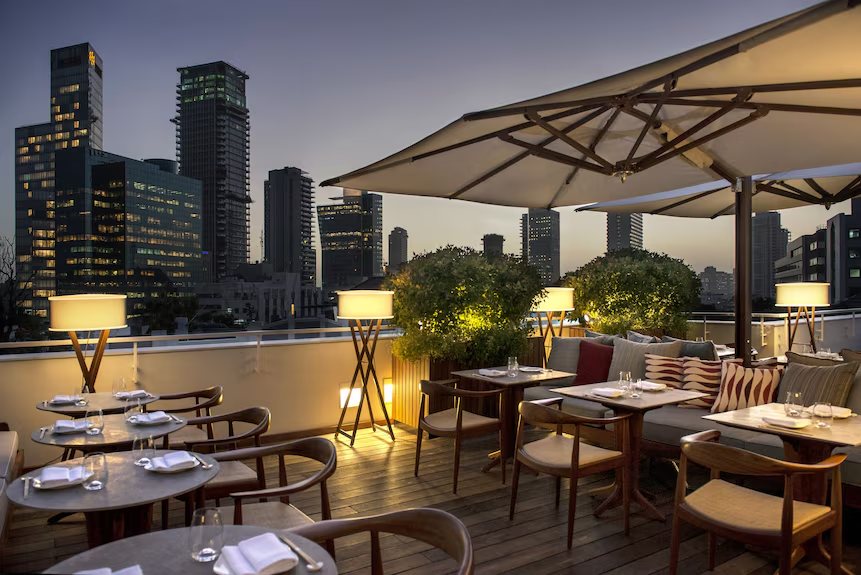 The rooftop dining terrace at The Norman at dusk, with the Tel Aviv skyline behind